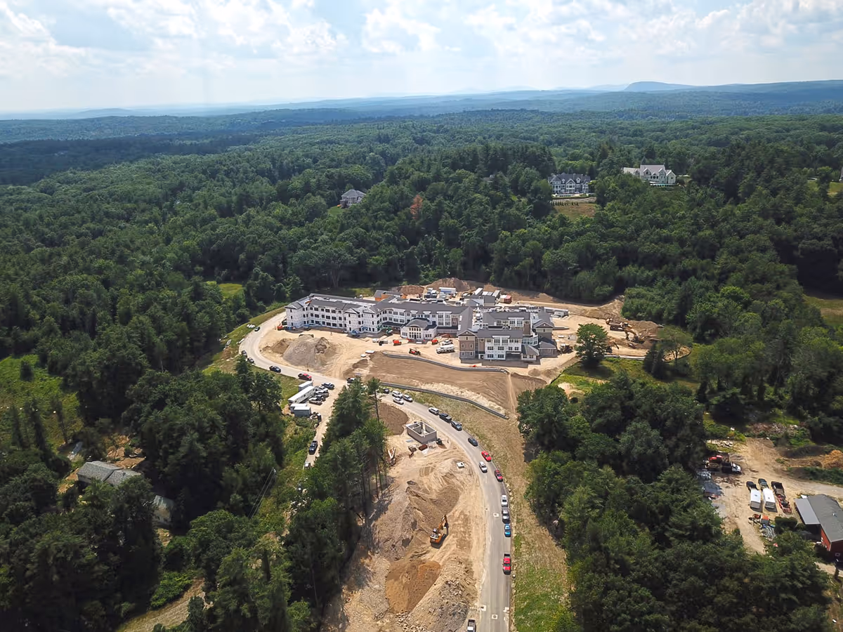 Aerial view of a large building complex under construction surrounded by dense forest and a winding access road.