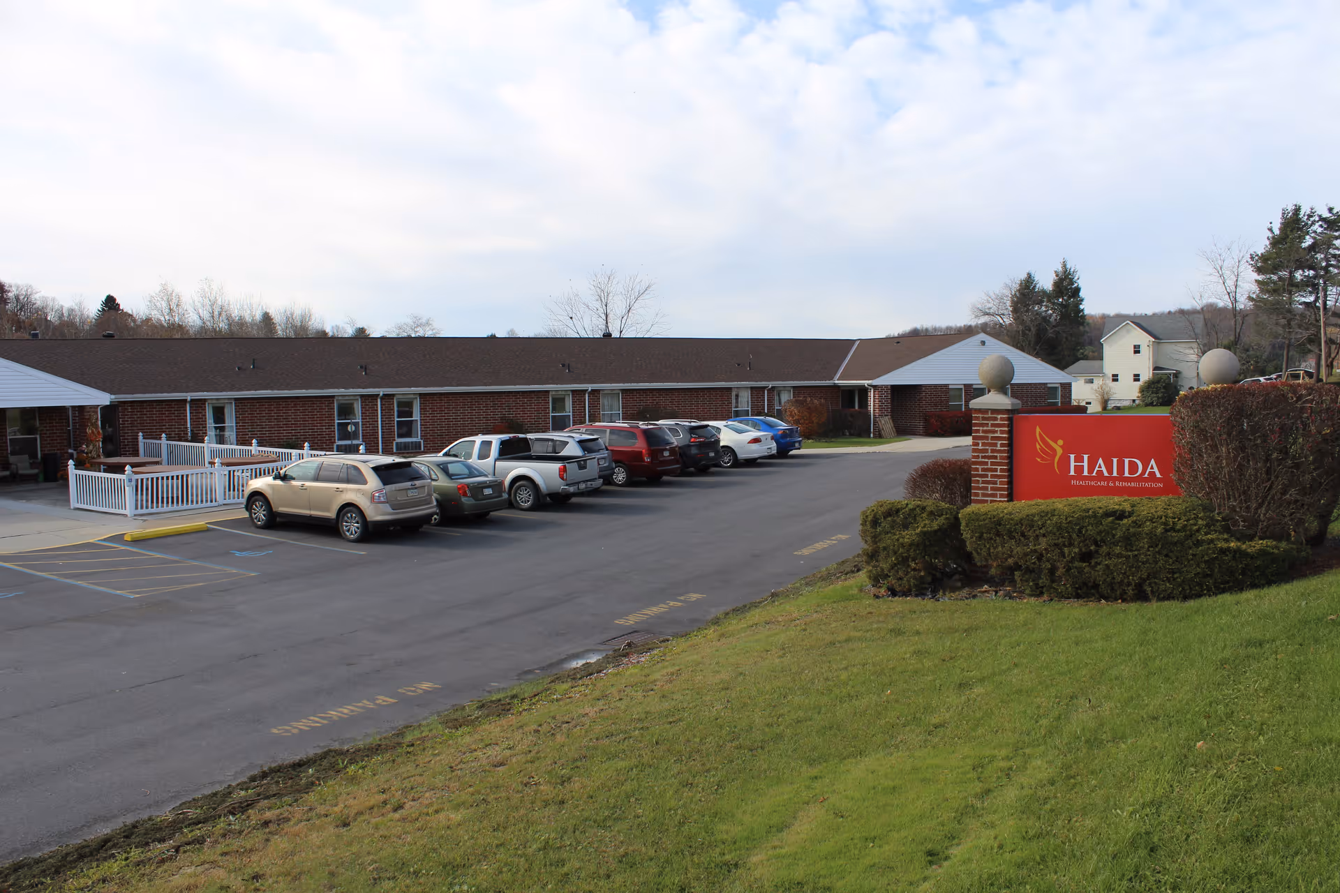 Front exterior of Haida Manor therapy department, a single-story brick building with a parking lot and a red entrance sign.
