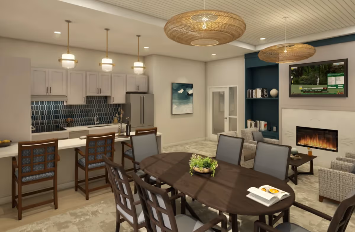 A modern open-concept living space featuring a kitchen with white cabinets, a dark blue tile backsplash, and three pendant lights above a breakfast bar with four wooden chairs. Adjacent to the kitchen is a dining area with a dark wooden oval table surrounded by six chairs, a small plant centerpiece, and an open book. In the background, there is a cozy sitting area with armchairs, a fireplace, built-in shelves, and a wall-mounted TV. The room has a light-colored ceiling with two large woven pendant lights and neutral-toned flooring.