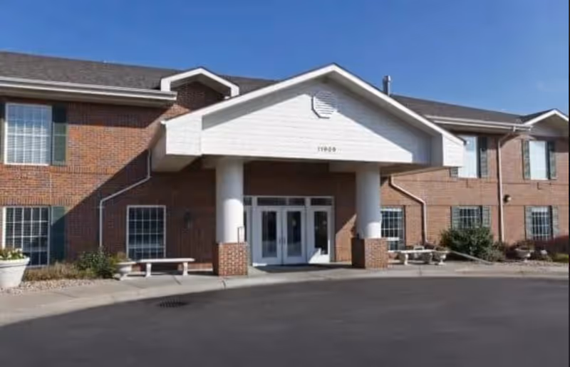 Brick senior living facility exterior with a covered entrance and benches.