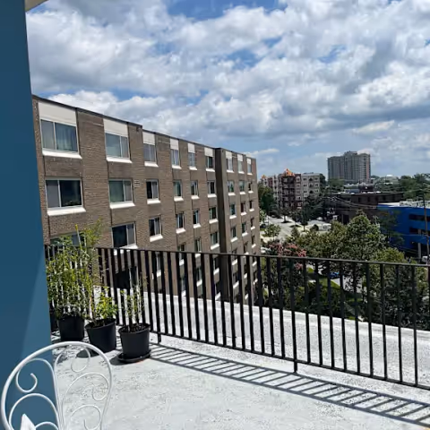 Outdoor balcony at Bethany House senior living, with a metal railing, potted plants, and a view of brick buildings and the cityscape.