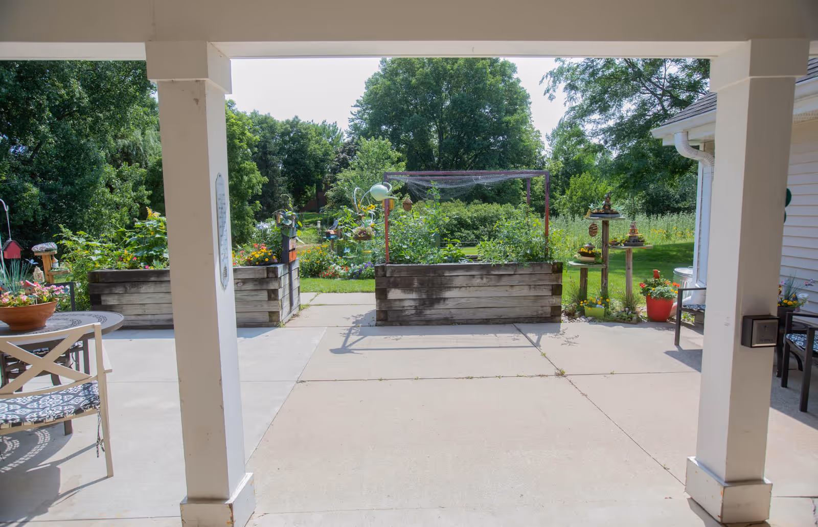 Covered patio looking out onto raised wooden garden beds, potted plants, and a grassy yard with trees.