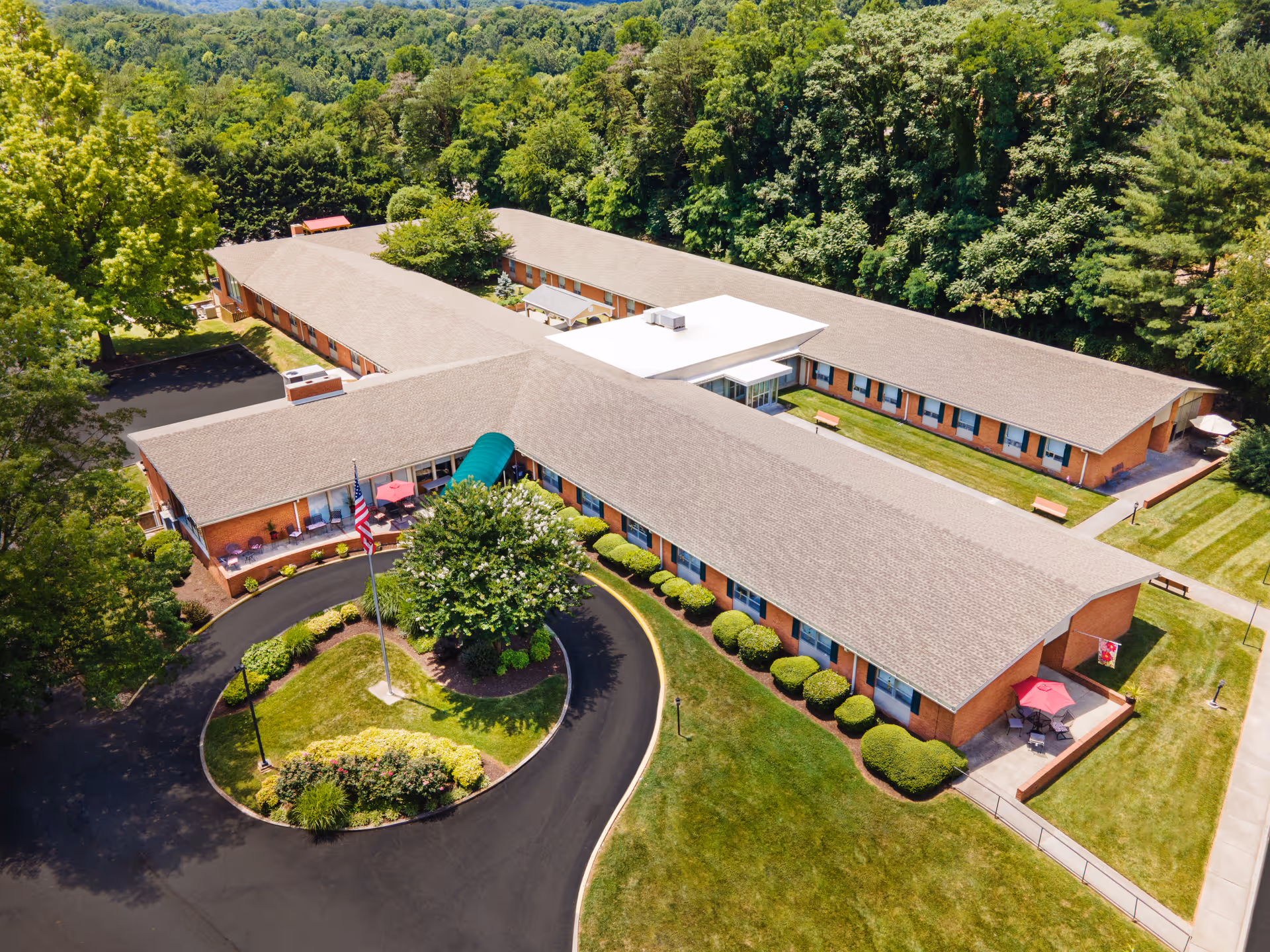 Aerial view of a single-story, U-shaped nursing home with a circular driveway, landscaped grounds, and surrounding trees.