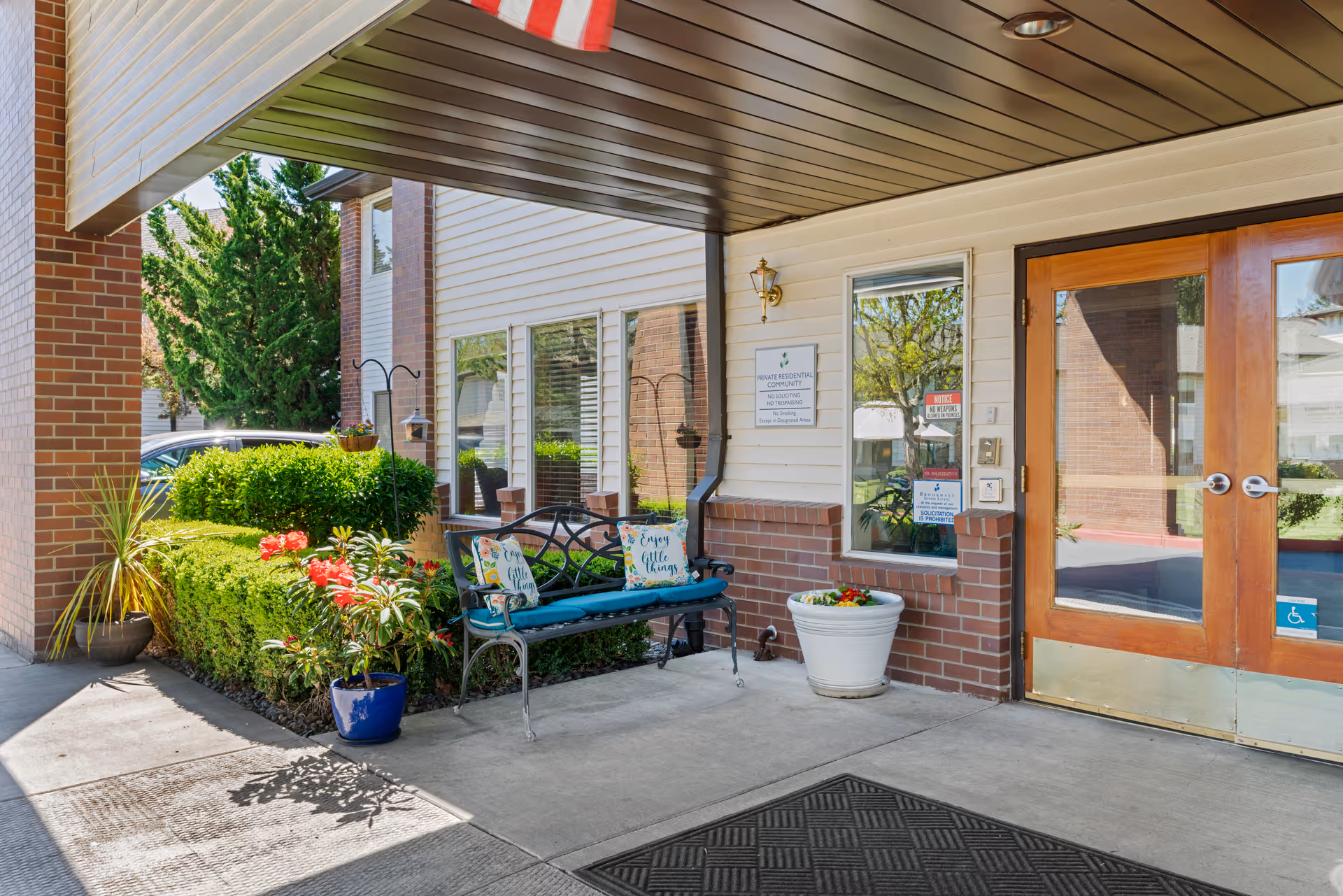 Covered entrance to Brookdale McMinnville City Center with double glass doors, a bench with colorful pillows, and potted plants.