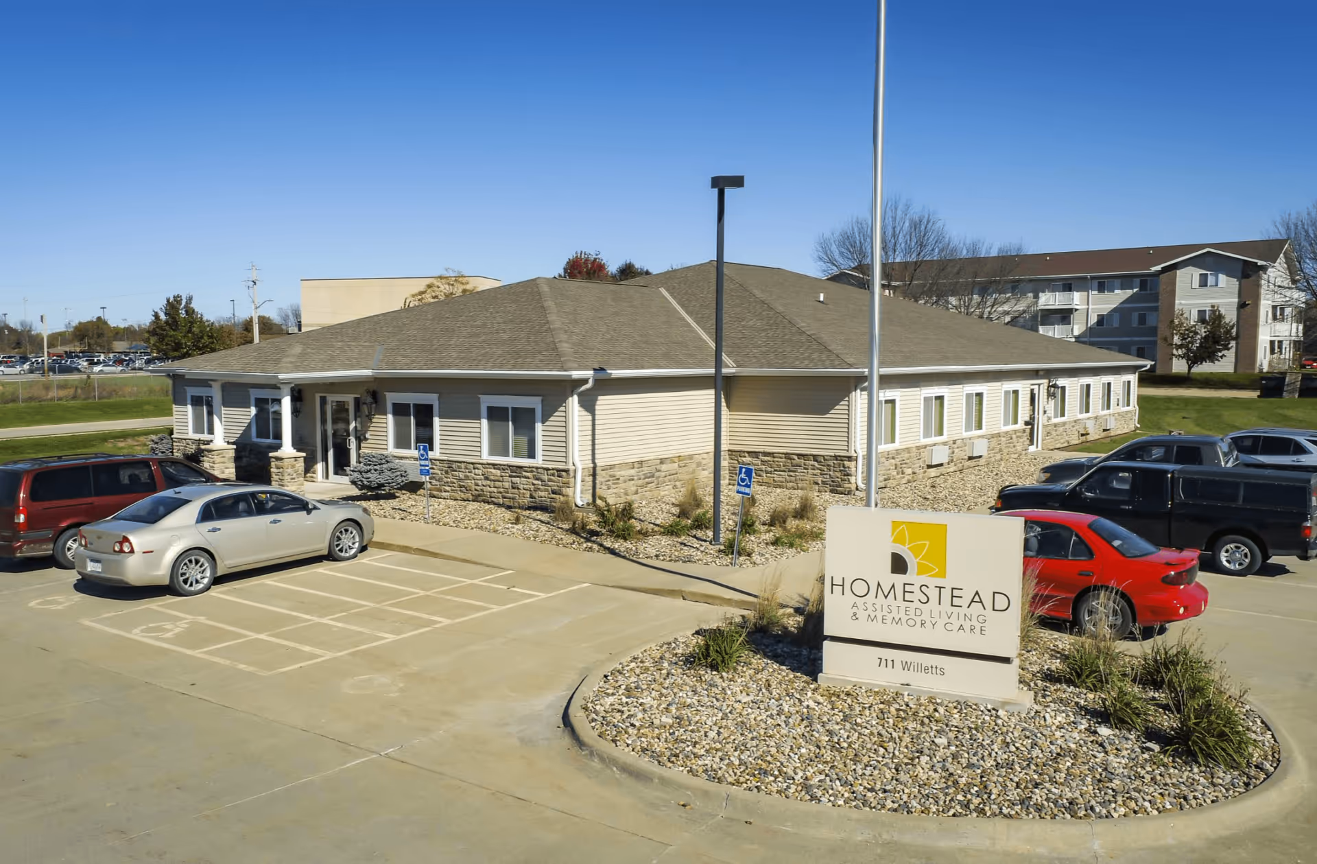Single-story beige assisted living building with a parking lot and a Homestead Assisted Living sign in front.