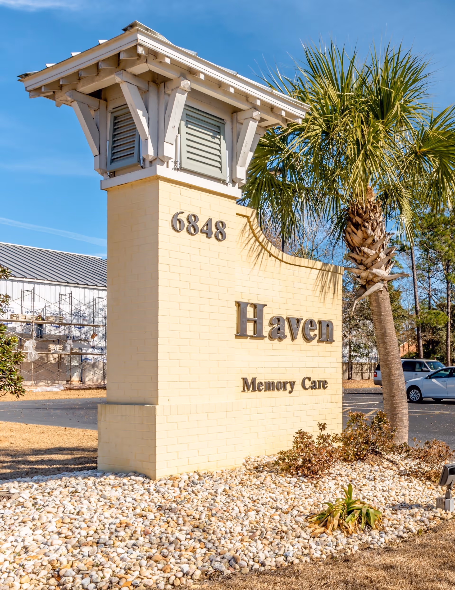 Brick entrance sign reading "Haven Memory Care" with the address number 6848, a palm tree, and a parking lot in the background.