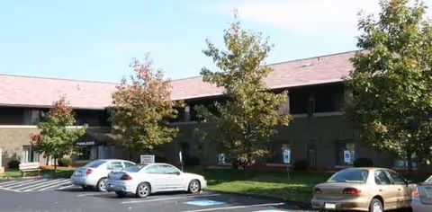 Senior living facility exterior with parked cars and trees along the front entrance.