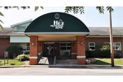 Front entrance of Hitz Memorial Home with brick facade, green canopy, and palm trees.