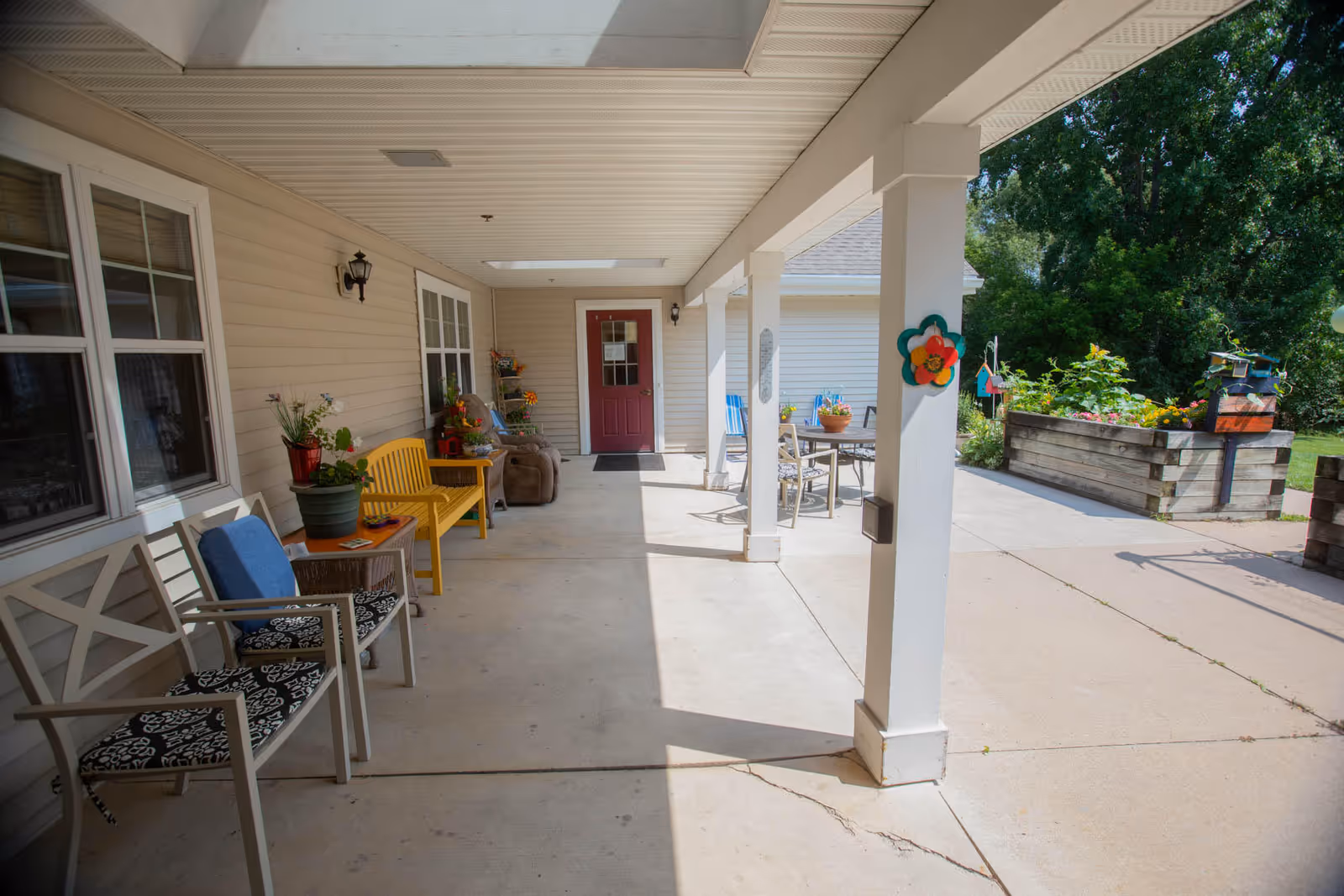 Covered porch entry with chairs, potted plants, raised planters, and a red door.