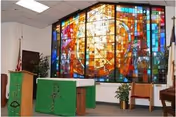 Interior chapel with a large colorful stained-glass window behind an altar and podiums draped in green cloth.