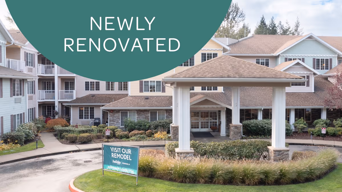 Exterior view of the Holiday Peninsula senior living facility showing a newly renovated building with a covered entrance, landscaped bushes, and a sign that reads 'Visit Our Remodel holiday Peninsula'.