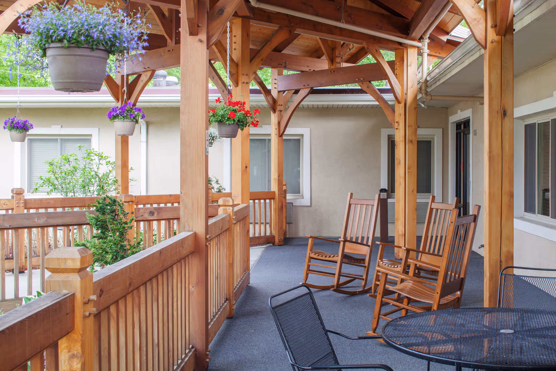 Covered wooden porch with hanging flower pots, several rocking chairs, and a metal patio table.