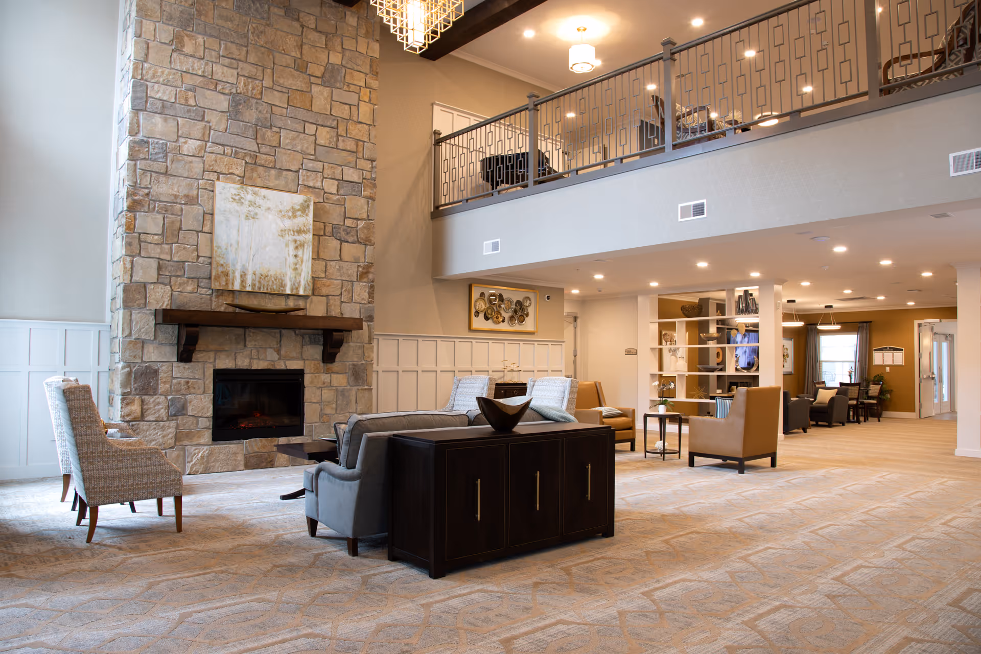 Open two-story lounge with a stone fireplace, seating areas, and a mezzanine balcony.