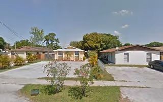 Exterior view of a senior living facility named Bimini Manor showing single-story buildings with driveways, small trees, and bushes under a clear blue sky.