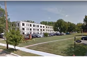 Exterior view of a multi-story rehabilitation and healthcare center building with a parking lot in front, surrounded by trees and green lawns under a clear sky.