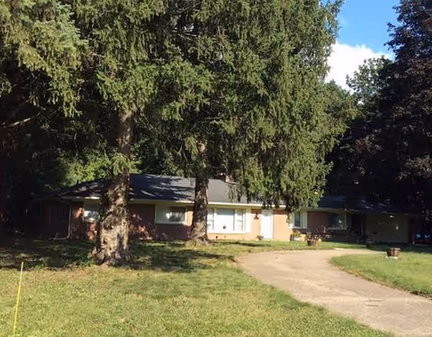 Front exterior of a single-story senior living facility with large trees.