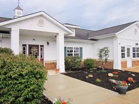 White single-story senior living facility exterior with entrance, walkway, and landscaping.