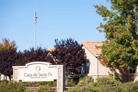 Exterior view of Casa de Santa Fe senior living facility with a stone sign and landscaping