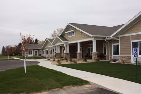 Exterior view of a senior living facility with a covered entrance, pillars, and a walkway.