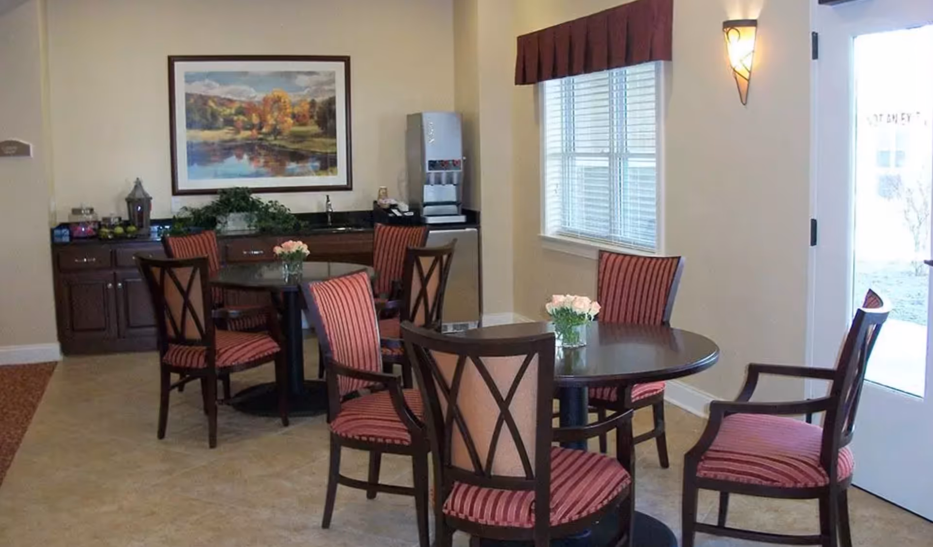 Small communal dining area with round tables, striped upholstered chairs, a beverage station, and wall art.