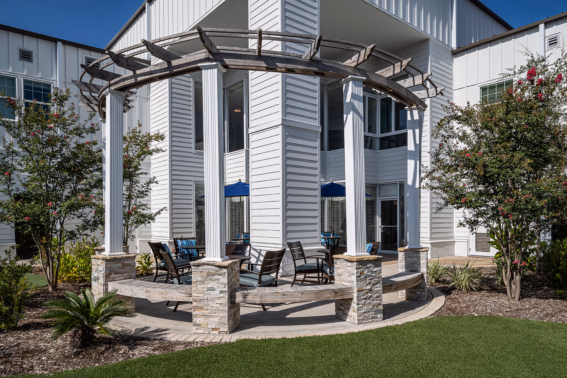 Outdoor courtyard at Meredith Court featuring a circular pergola with white columns and patio seating in front of a white multi-story building.