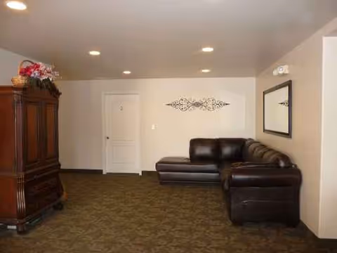 Neutral-tone living room in a senior facility with a leather sectional and cabinet.