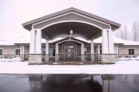 Front entrance of a single-story building with a covered porte-cochere, stone columns and snow on the ground.