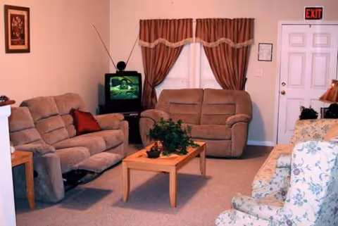 Cozy beige living room with sofas, a coffee table, plant, and a TV.