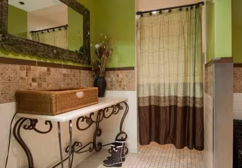 Green-walled bathroom with ornate metal vanity, wicker basket, and patterned shower curtain.