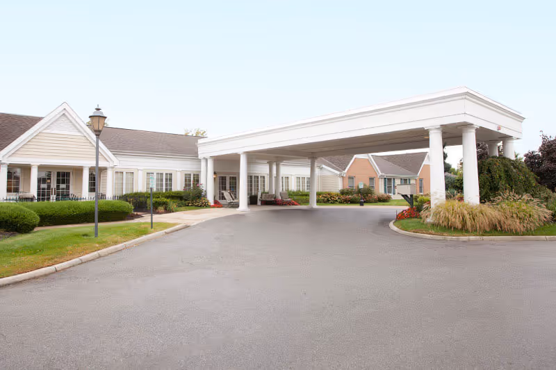 Front entrance of a single-story senior living facility with a covered porte-cochere and driveway.