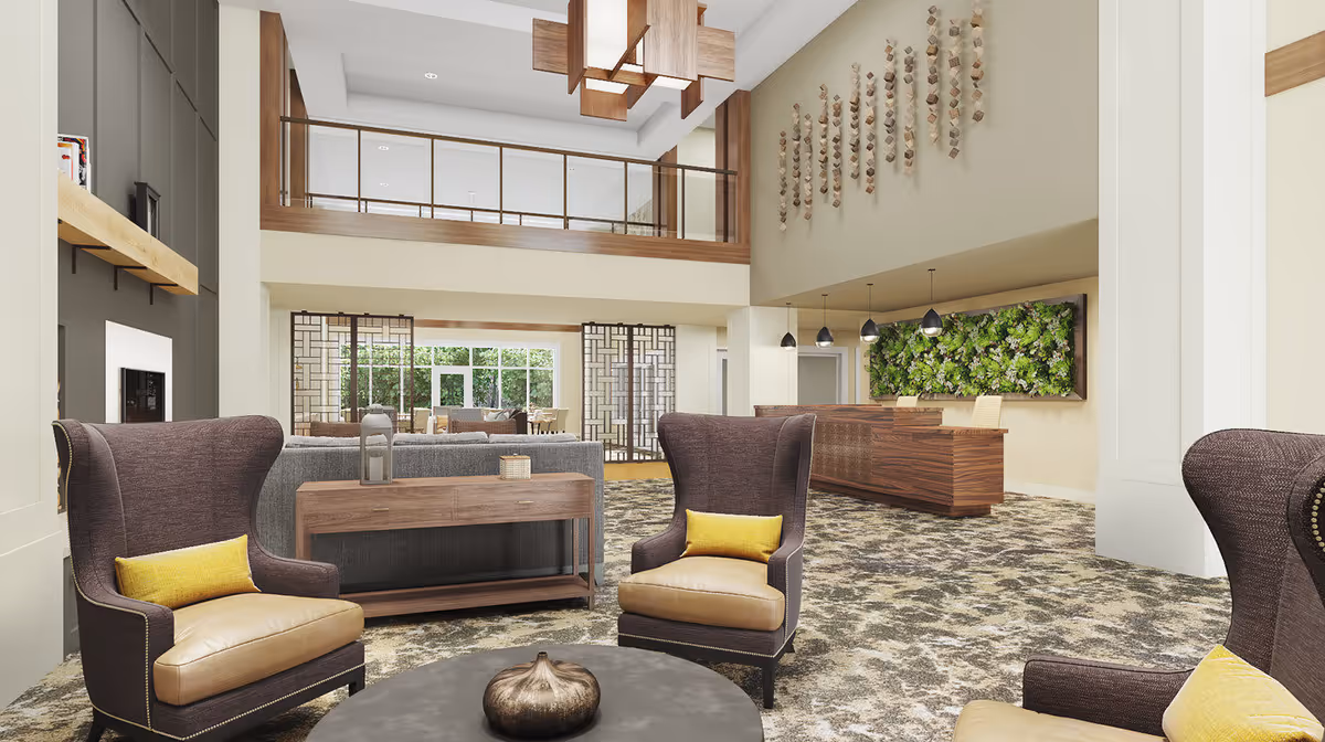 Spacious and well-lit senior living facility common area with high ceilings, featuring comfortable armchairs with yellow cushions, a round coffee table with a decorative item, a wooden console table behind a gray sofa, a reception desk with pendant lights, and a green vertical garden on the wall.