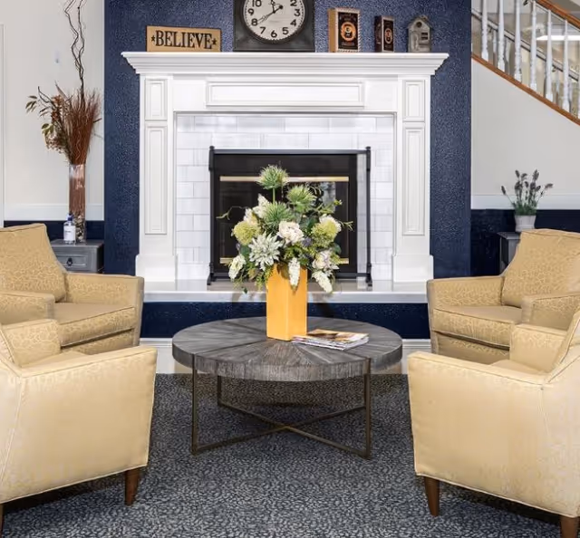 Cozy seating area with four armchairs around a round coffee table and a floral arrangement in front of a white fireplace.