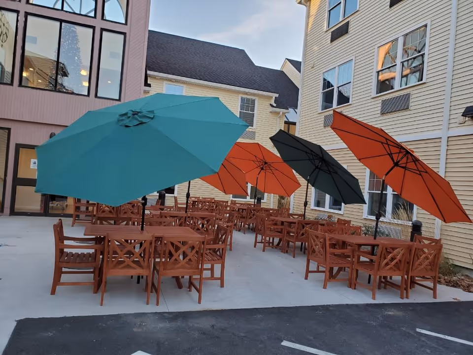 Outdoor patio with wooden tables and colorful umbrellas set beside a senior living building.