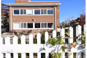 Two-story brick nursing facility with a white picket fence and outdoor seating.