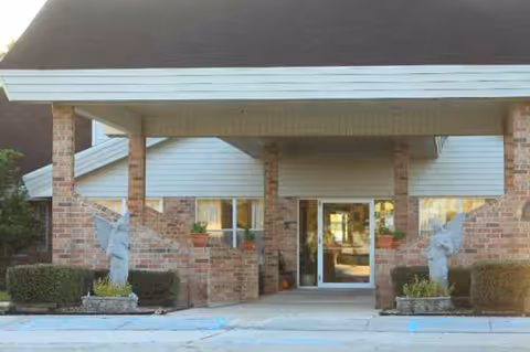 Brick facility entrance with a covered drop-off, glass doors, planters, and statues.