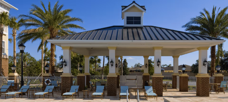 Outdoor poolside pavilion with lounge chairs and palm trees under a clear blue sky.
