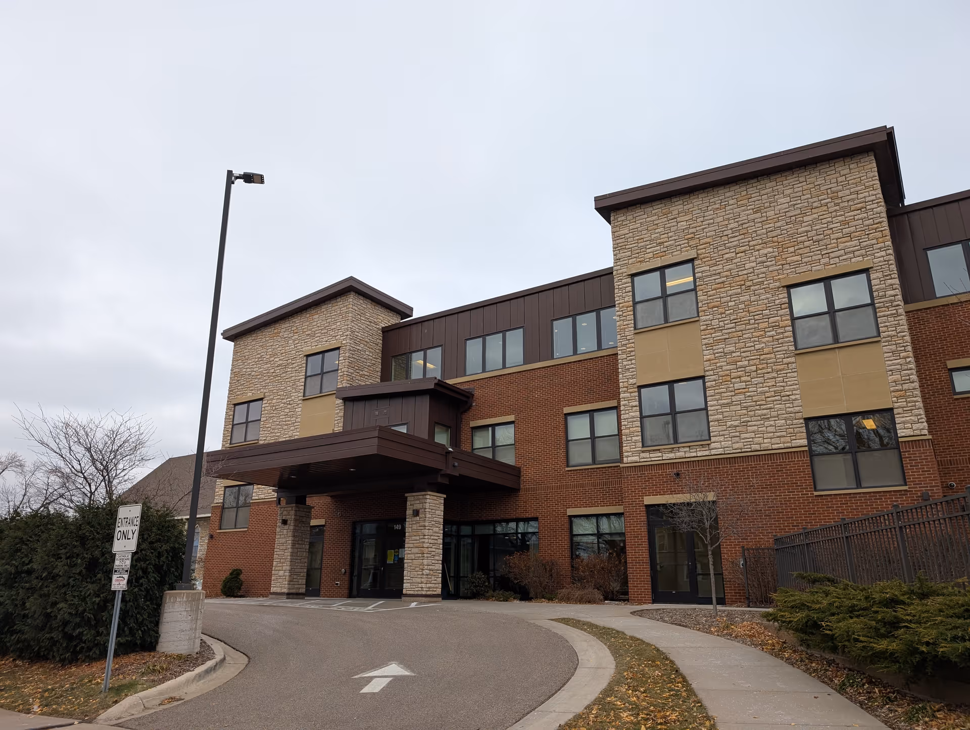Front entrance of a three-story brick and stone senior living facility with a covered porte-cochère and driveway.