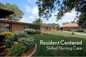 Outdoor view of a single-story brick building with well-maintained landscaping including green grass, bushes, and flowers under a partly cloudy sky. Text on the image reads 'Resident Centered Skilled Nursing Care.'