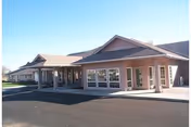 Single-story brick senior living building with a covered entrance, large windows, and a paved driveway under a clear sky.