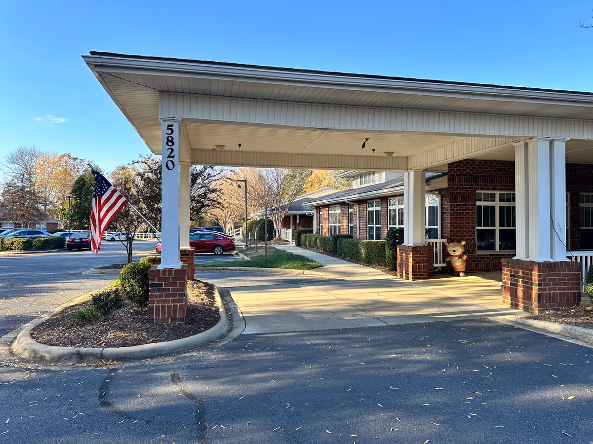 Covered entrance/portico of a brick senior living building with the address 5820, an American flag, and a parking lot.
