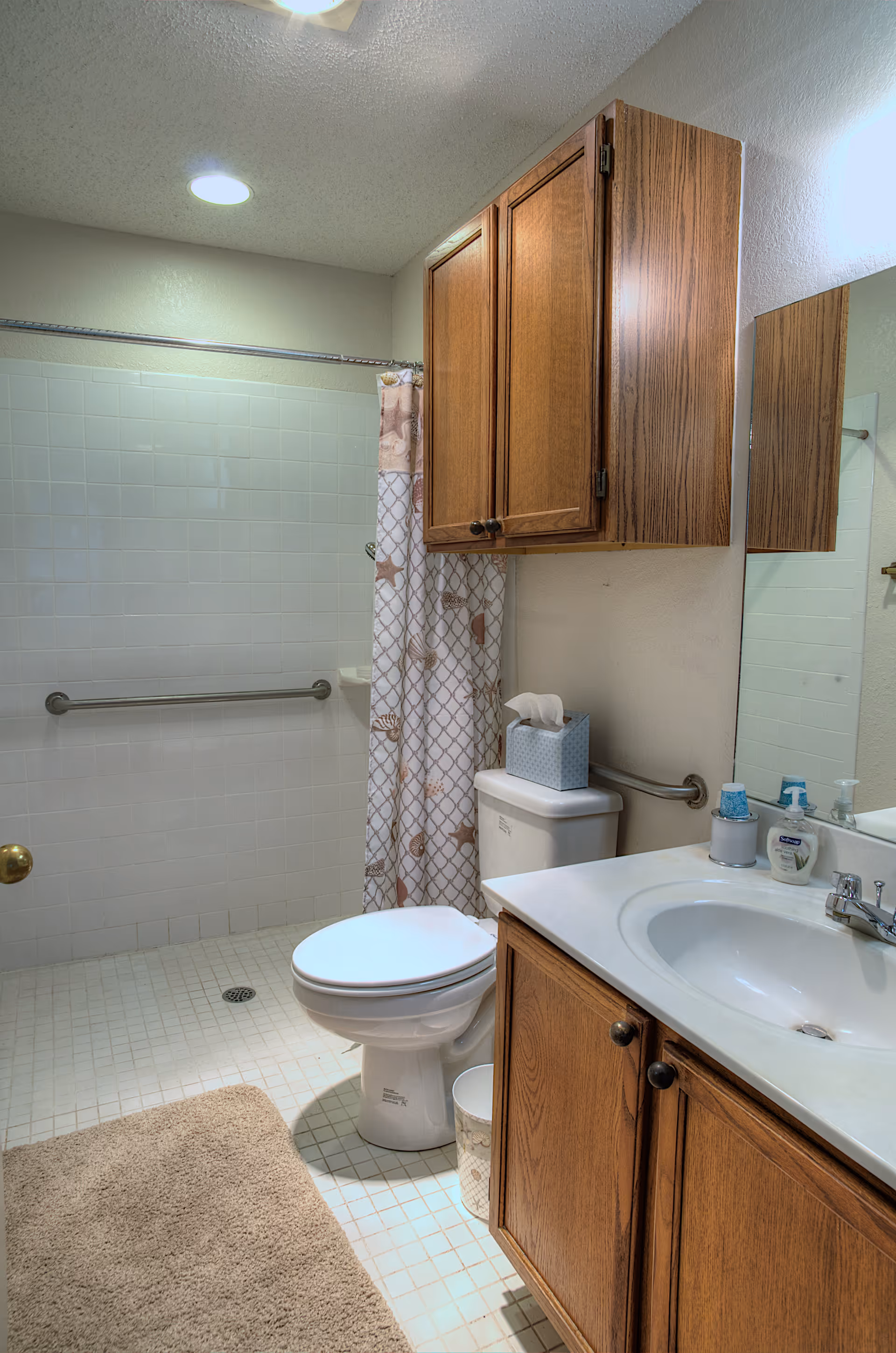 Bathroom featuring a toilet, sink with vanity, wooden cabinets, and a shower with a grab bar and patterned curtain.