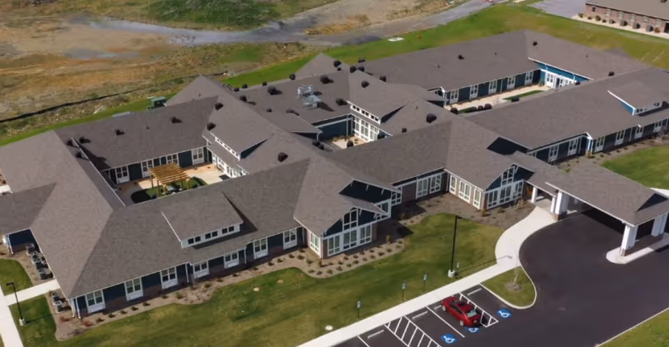 Aerial view of the English Meadows Fishersville senior living facility: a U-shaped single-story building with a covered entrance, central courtyards, parking spaces, and surrounding lawn.