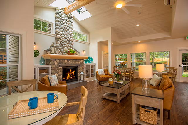 Open, bright communal living area featuring a stone fireplace, leather seating, wooden floors, dining tables, and skylights.