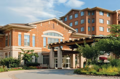 Front entrance of a multi-story brick senior living community with a covered porte-cochere and landscaped grounds.