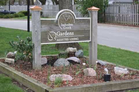 Wooden sign reading Imboden Creek Gardens Assisted Living in a landscaped front yard.