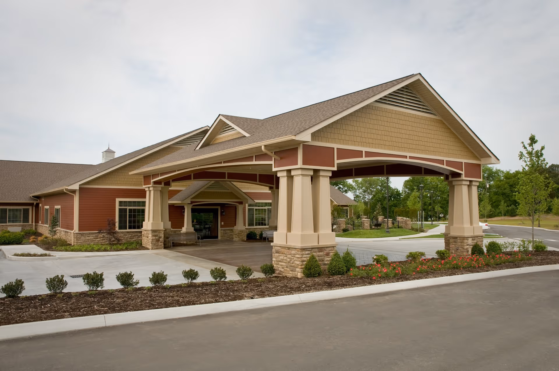 Covered entrance canopy and front facade of a one-story senior living facility with landscaped beds and a driveway.