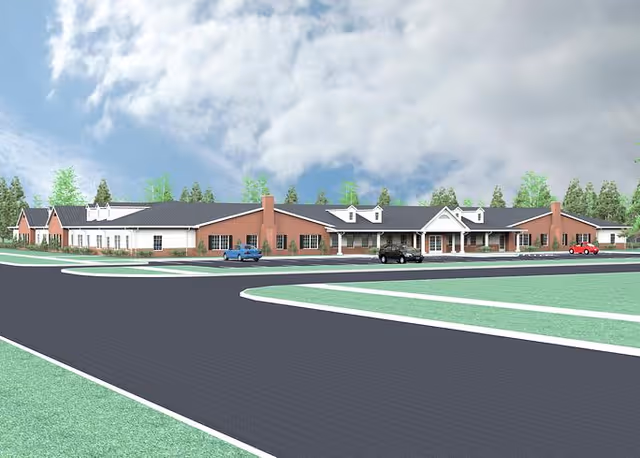 A wide exterior view of a single-story senior living community building with a brick and white facade, multiple chimneys, and a covered entrance. The building is surrounded by a paved road and green landscaping with trees in the background under a partly cloudy sky.