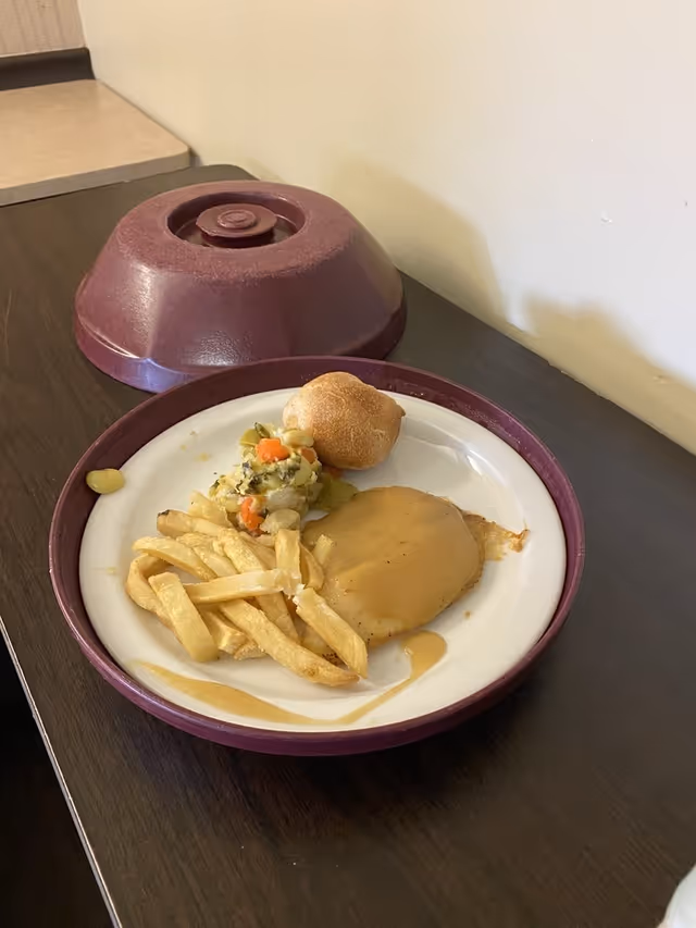 Plate of fries with vegetables, roll, and gravy on a dining table.