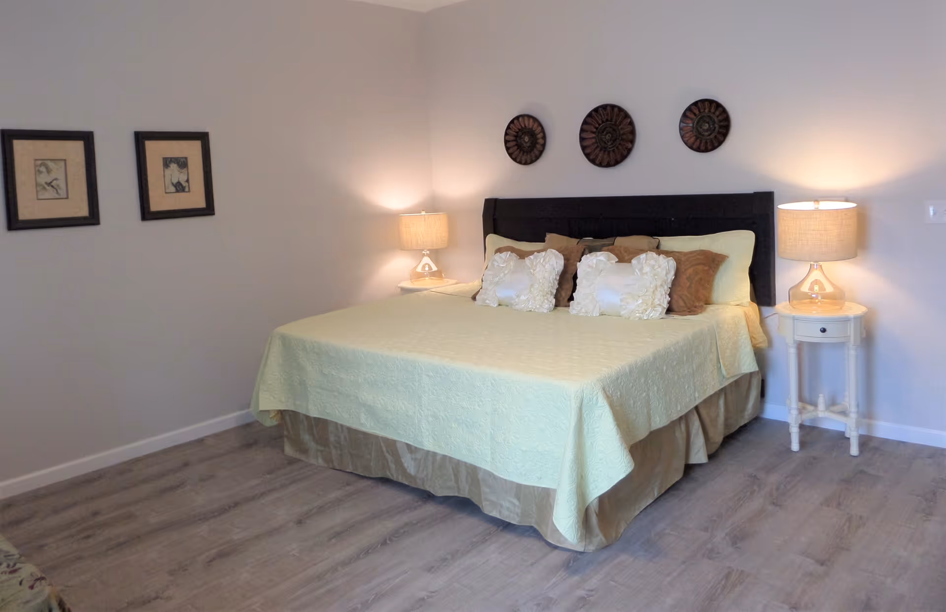 Neatly made bed with decorative pillows, two bedside tables with lamps, and wall decor in a bright bedroom.