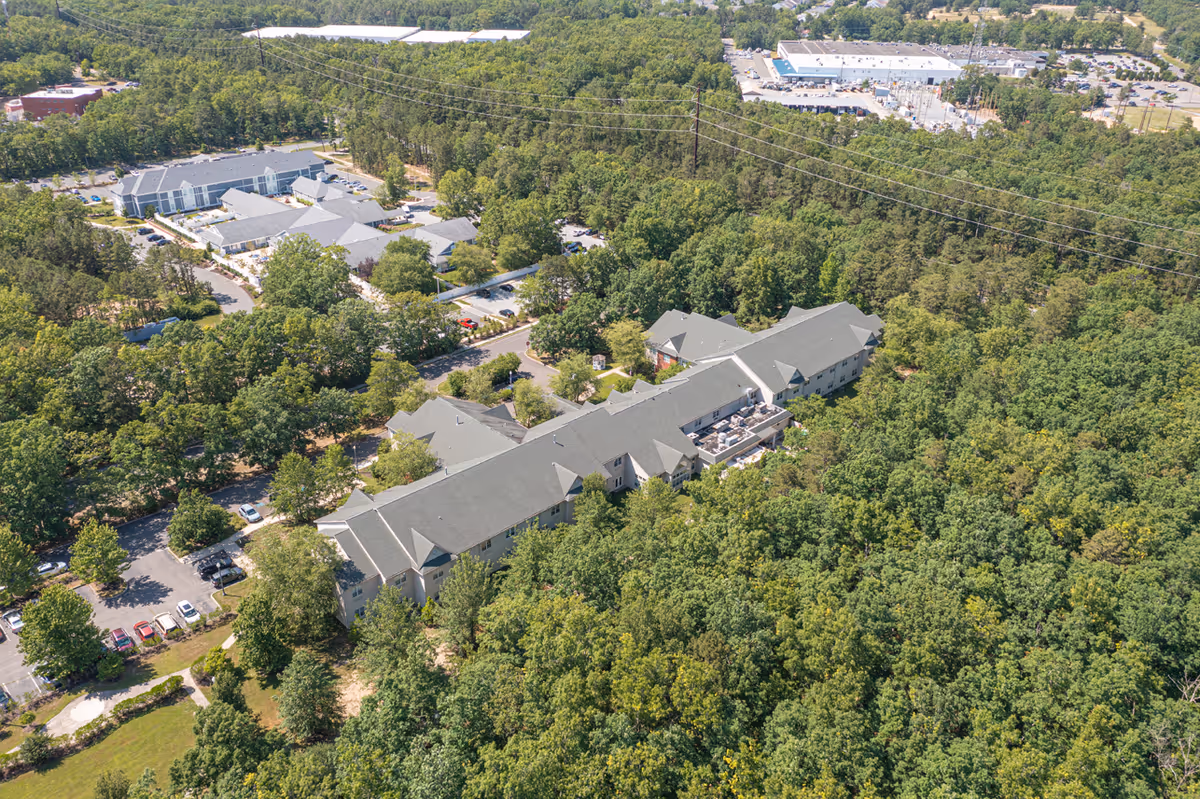 Aerial view of a long multi-wing senior living facility surrounded by dense trees and parking areas.
